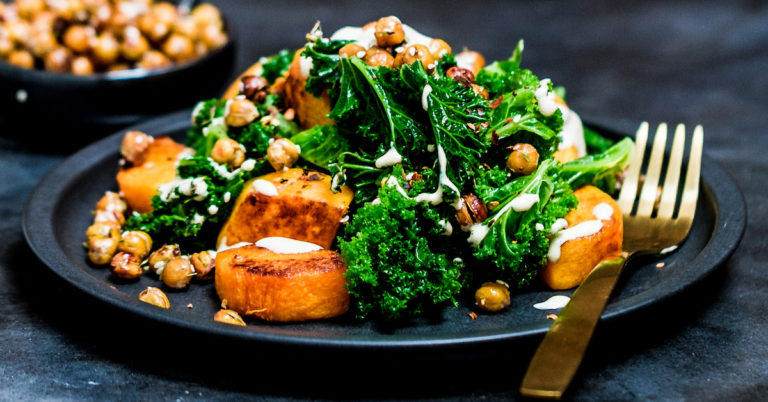 Baked butternut squash cubes with steamed kale, crispy chickpeas and tahini sauce on a black plate