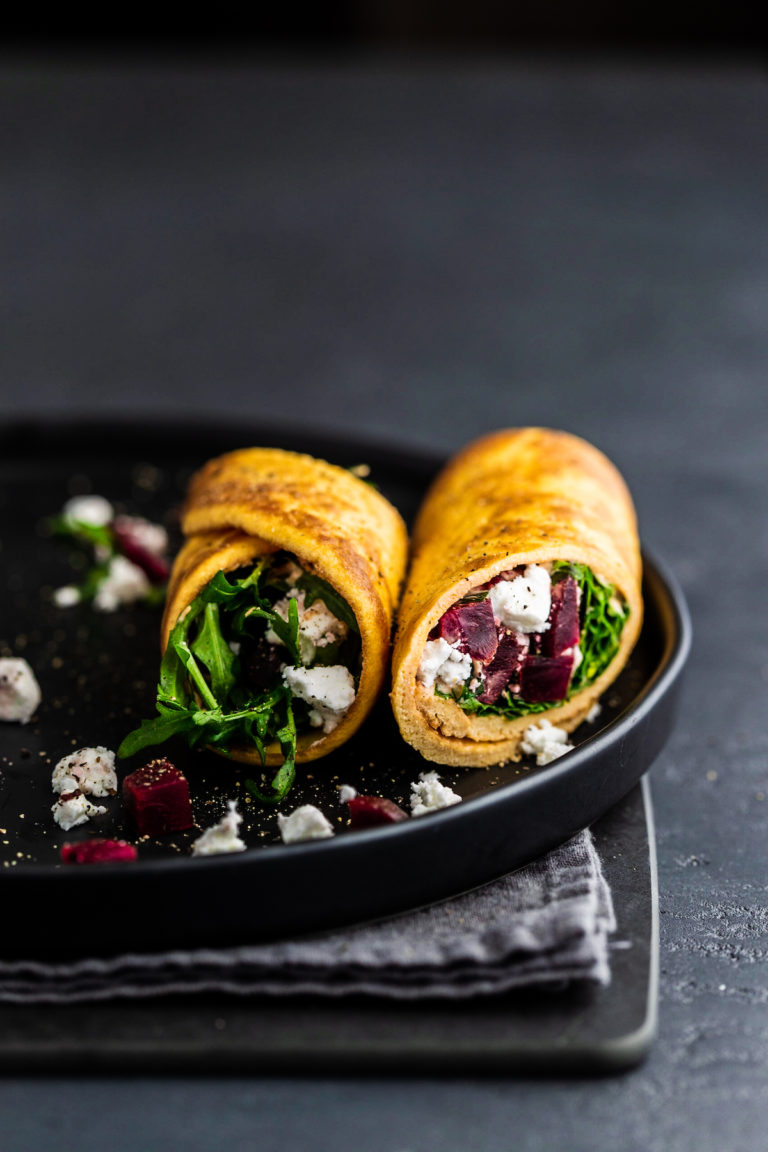 Breakfast egg wraps with goat cheese and beet, on a black plate
