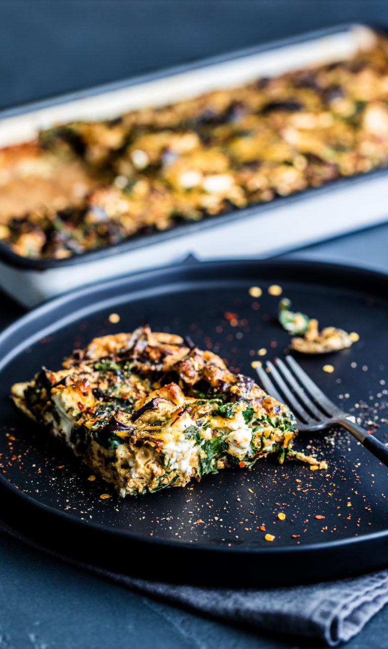 One piece of frittata from a tray, on a black plate with a fork