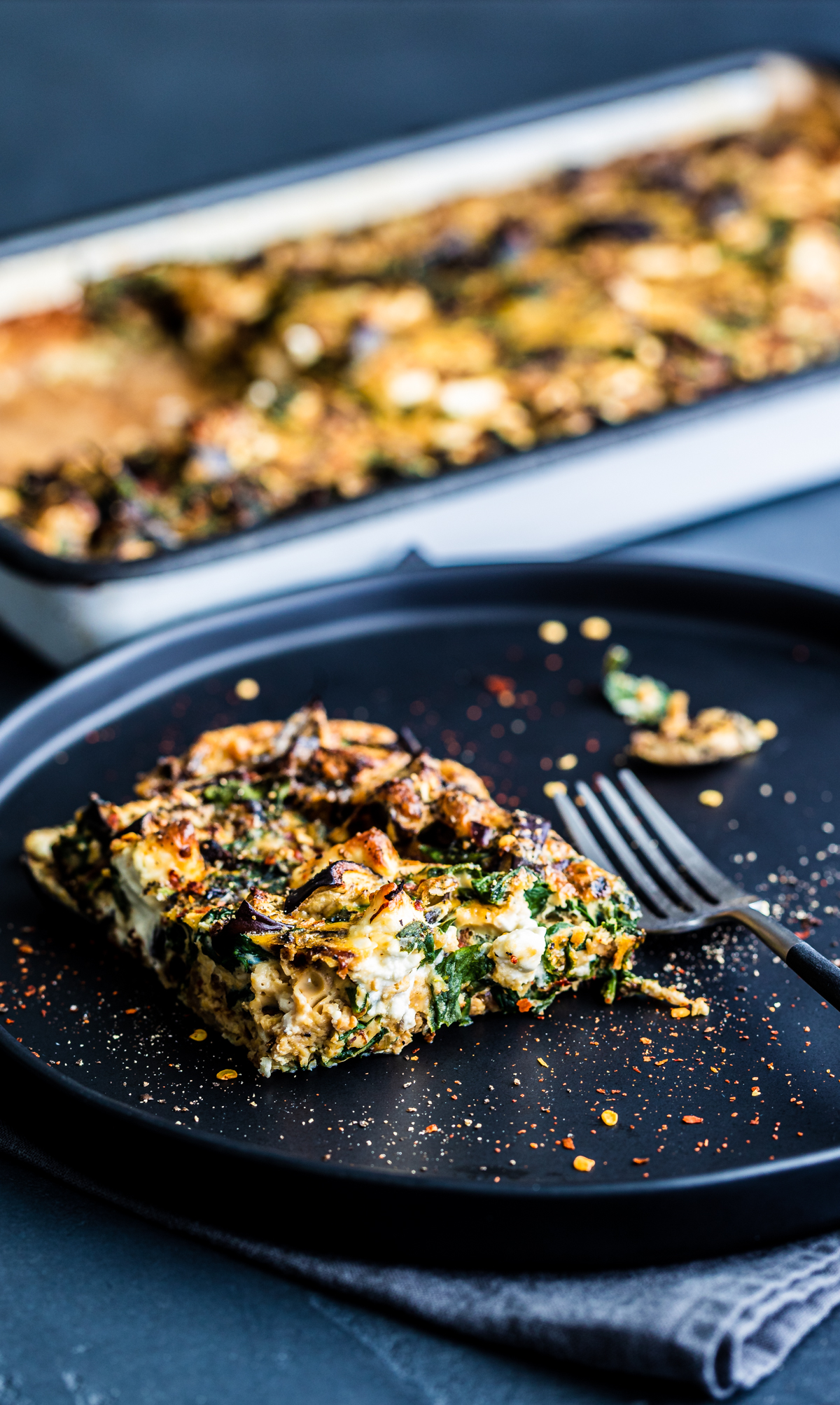 One piece of Caramelised Onion & Feta Frittata from a tray, on a black plate with a fork