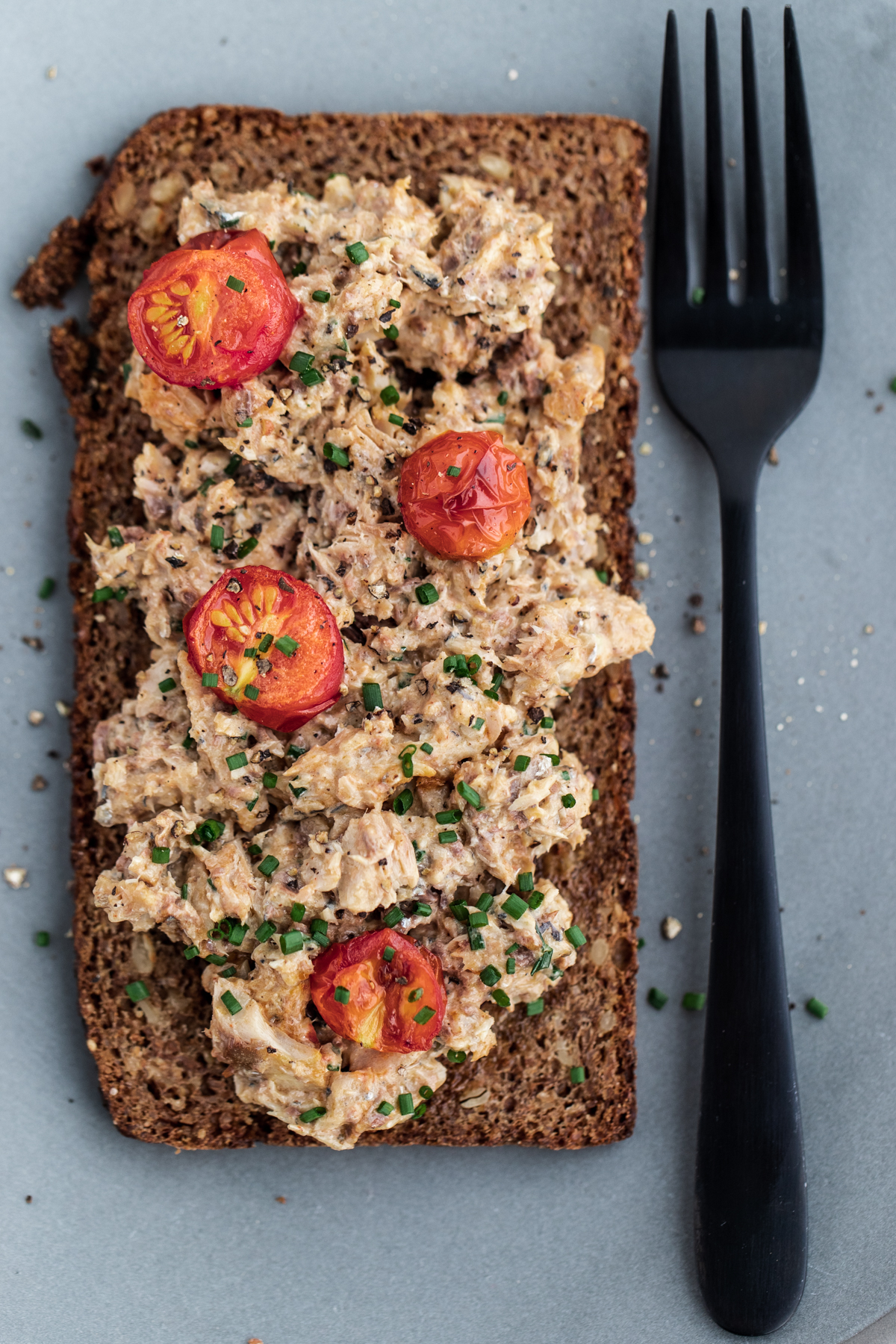 Open faced sardine mayo sandwich on rye bread on a blue plate with a black fork