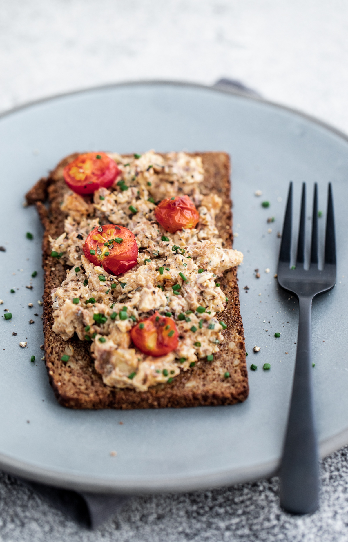 Open faced sardine mayo sandwich on rye bread on a blue plate with a black fork