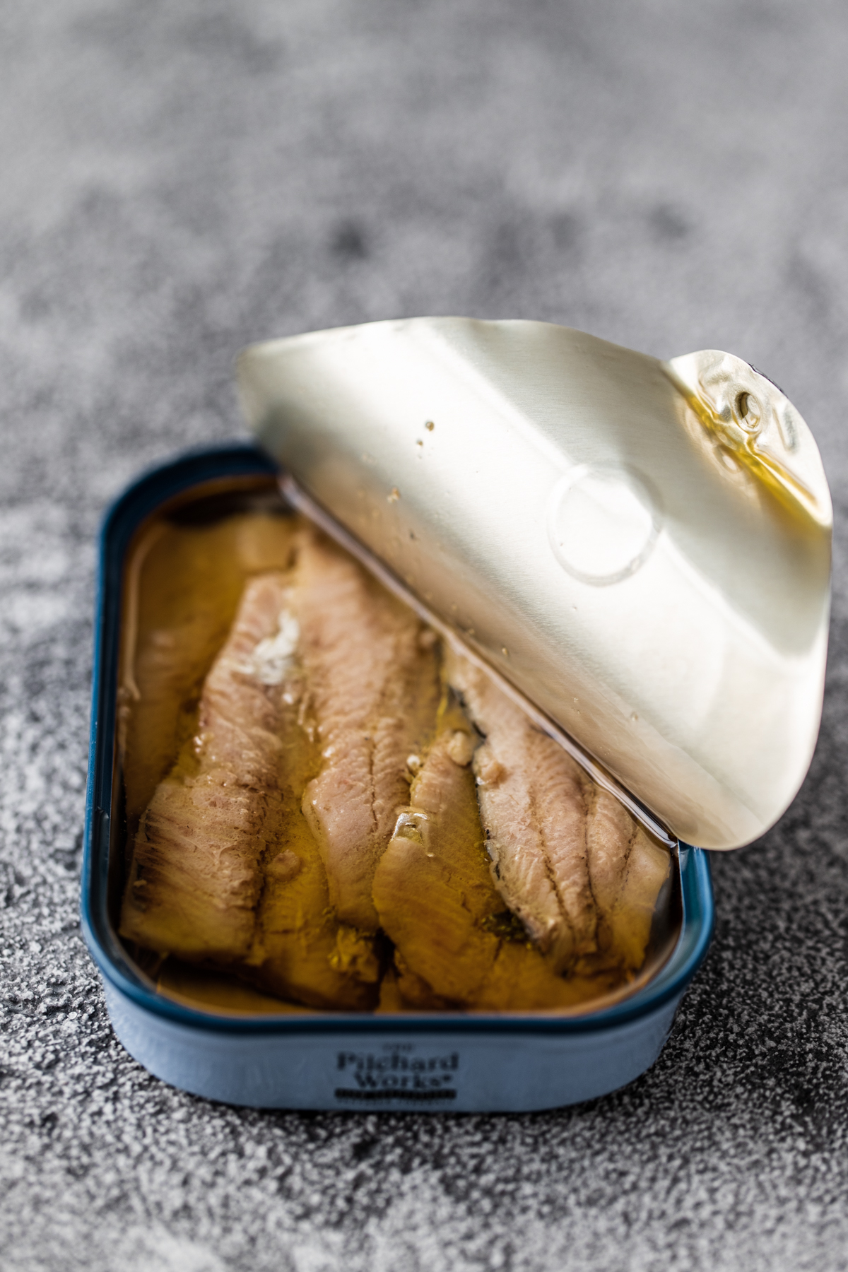 Sardine fillets in a blue tin with the lid half peeled back on a grey black background