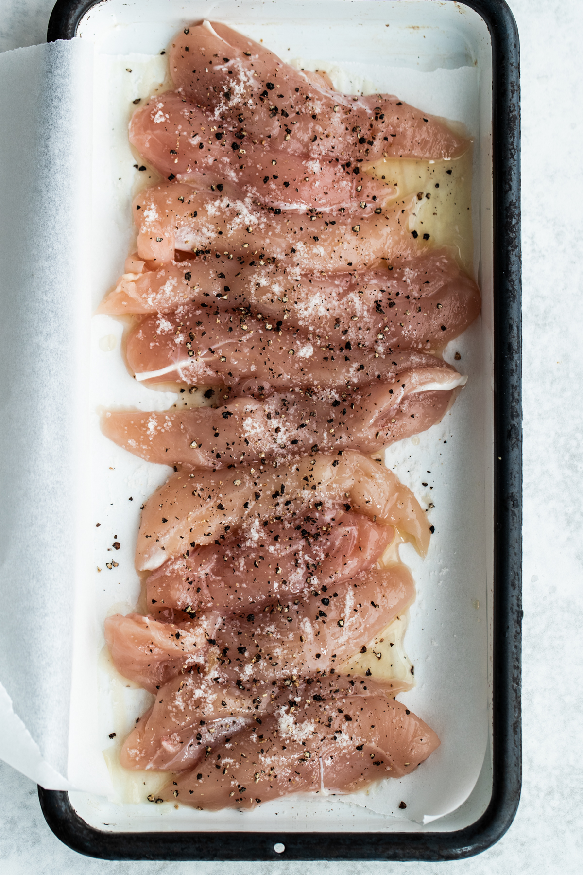 Overhead view of lemon pepper chicken breast mini-fillets on a white baking pan lined with parchment