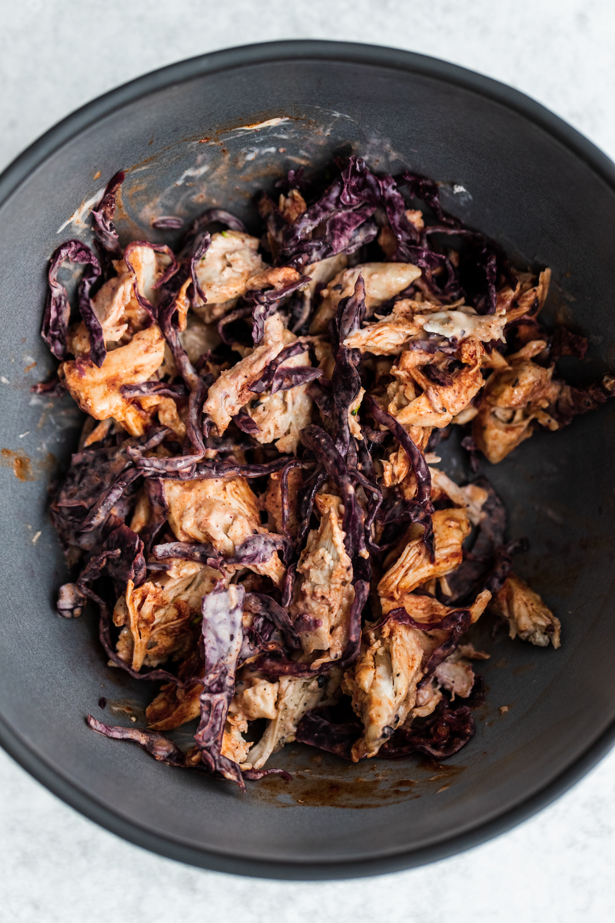 Overhead shot of shredded chicken, red cabbage sauerkraut and hot sauce mayo in a bowl.