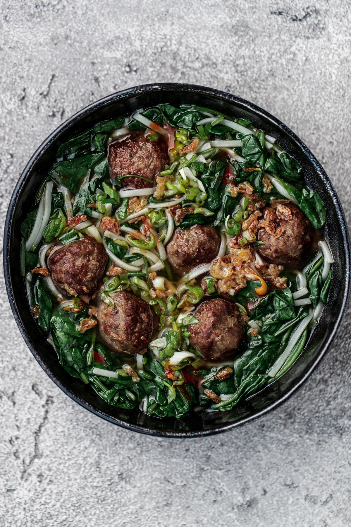 A bowl of easy meatball pho in a black bowl on a grey background