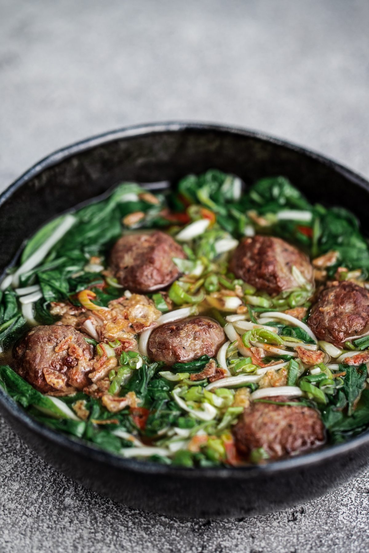 A bowl of easy meatball pho in a black bowl on a grey background