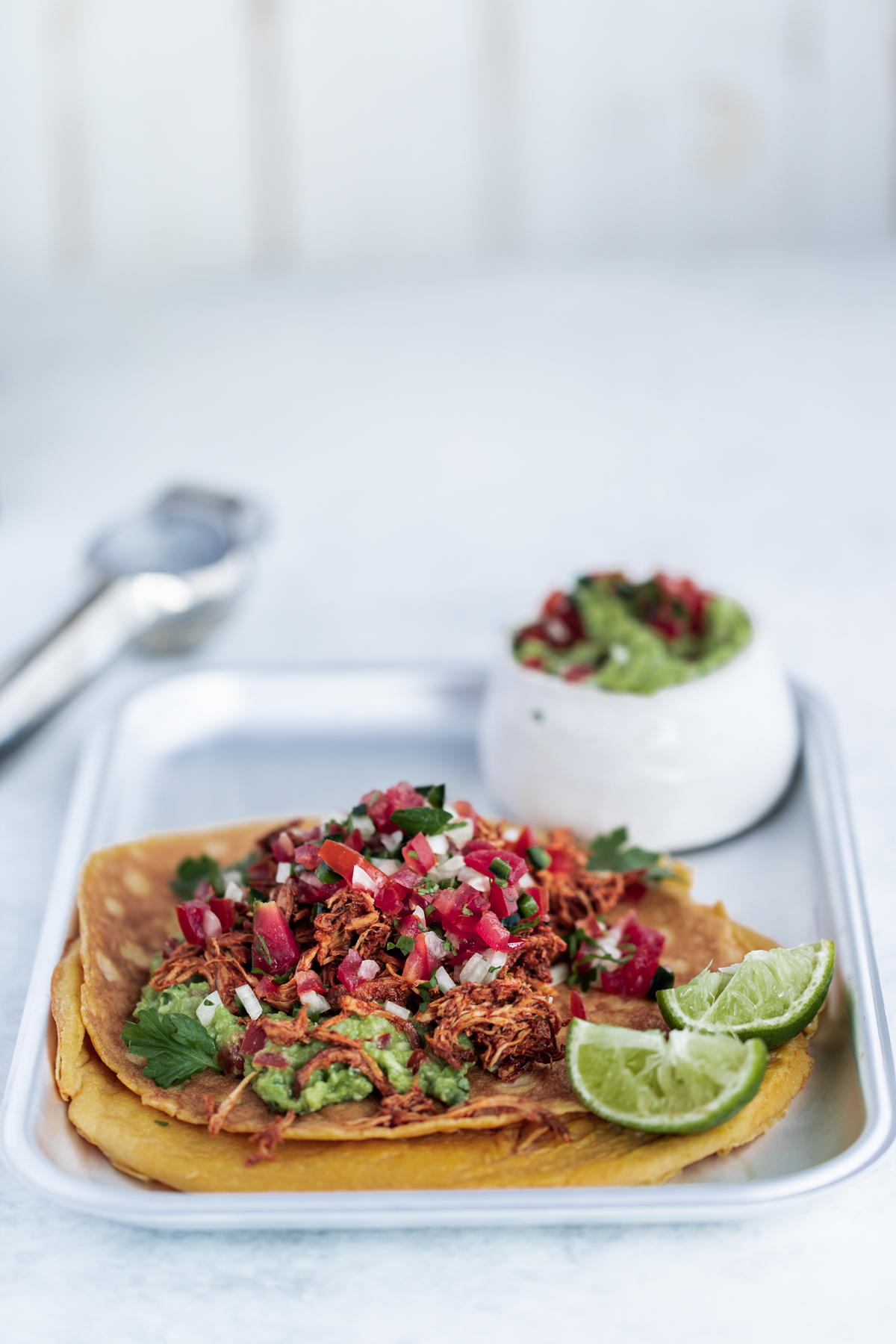 Slow cooked chipotle chicken egg wraps with lime, pico de gallo and guacamole on a silver tray and white background.