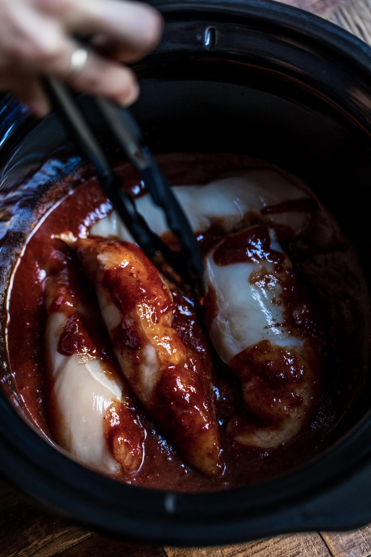 Chicken breasts being put into the chipotle sauce in a slow cooker with tongs 