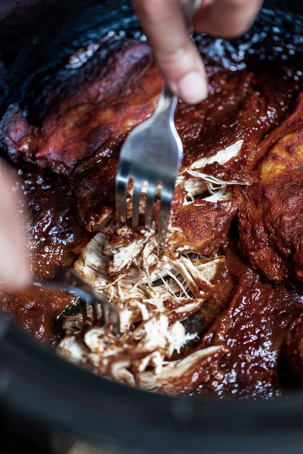 Slow cooked chipotle chicken in a slow cooker being shredded with forks