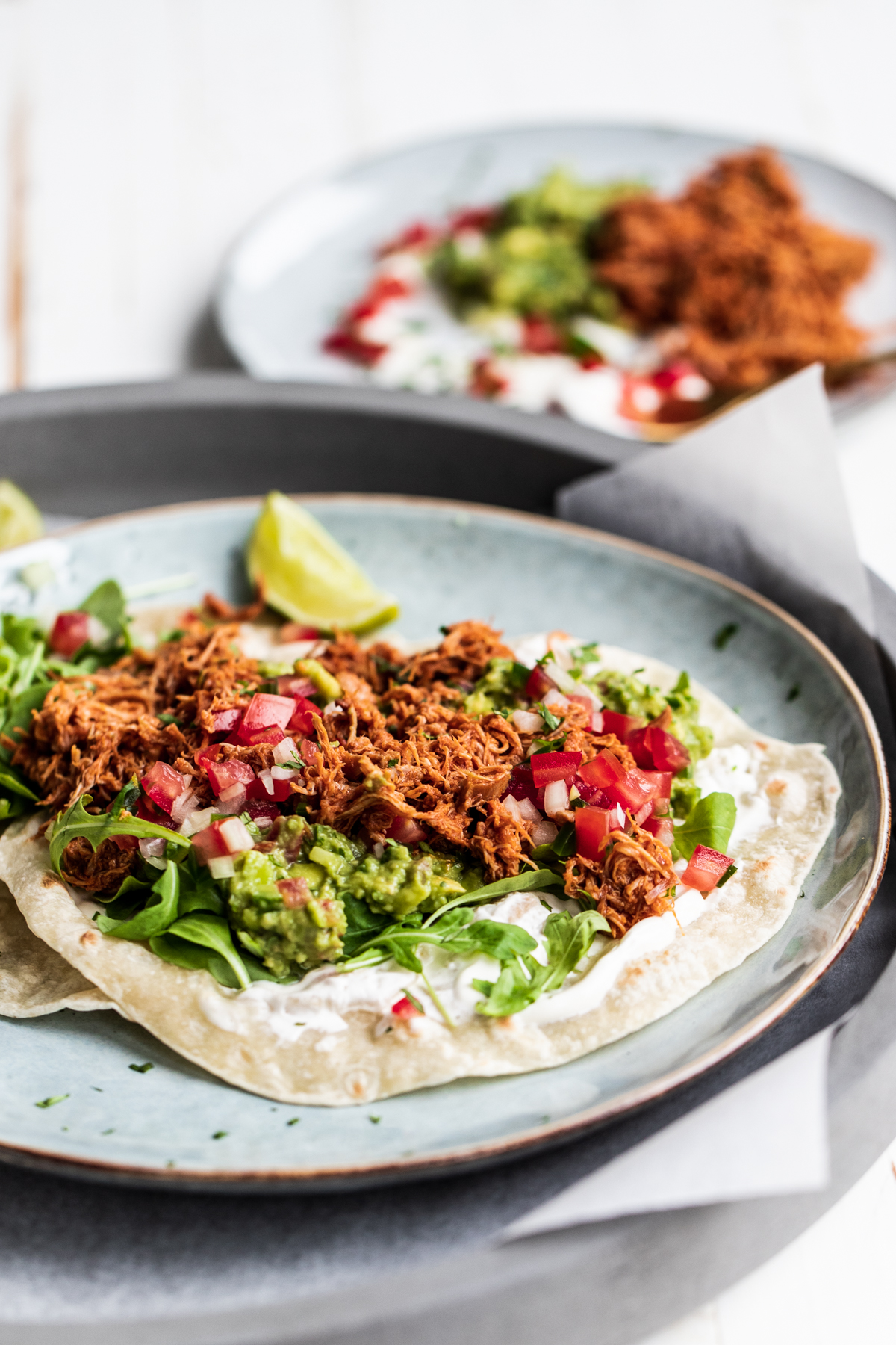 Slow cooked chipotle chicken tacos on a blue plate and white background