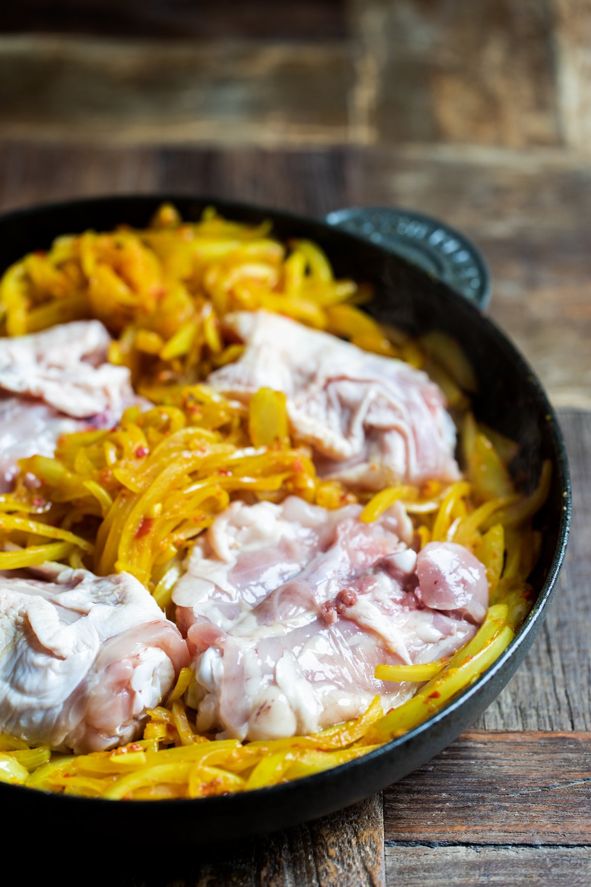 Onions and chicken thigh with Malaysian curry paste cooking in a black cast iron pan.