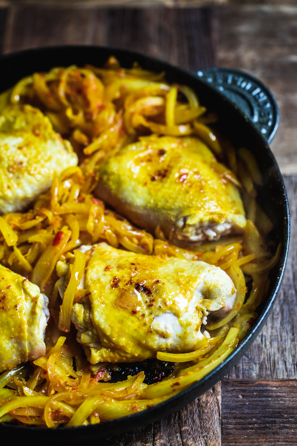 Onions and chicken thigh with Malaysian curry paste cooking in a black cast iron pan.