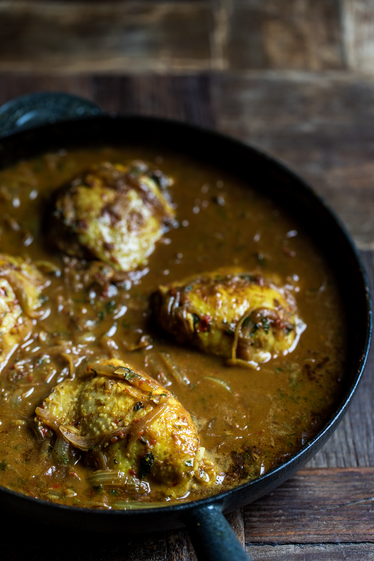Malaysian chicken thigh curry cooking in a black cast iron pan.