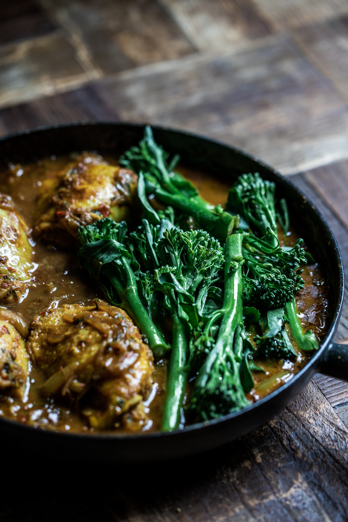 Malaysian chicken thigh curry cooking in a black cast iron pan with broccoli.