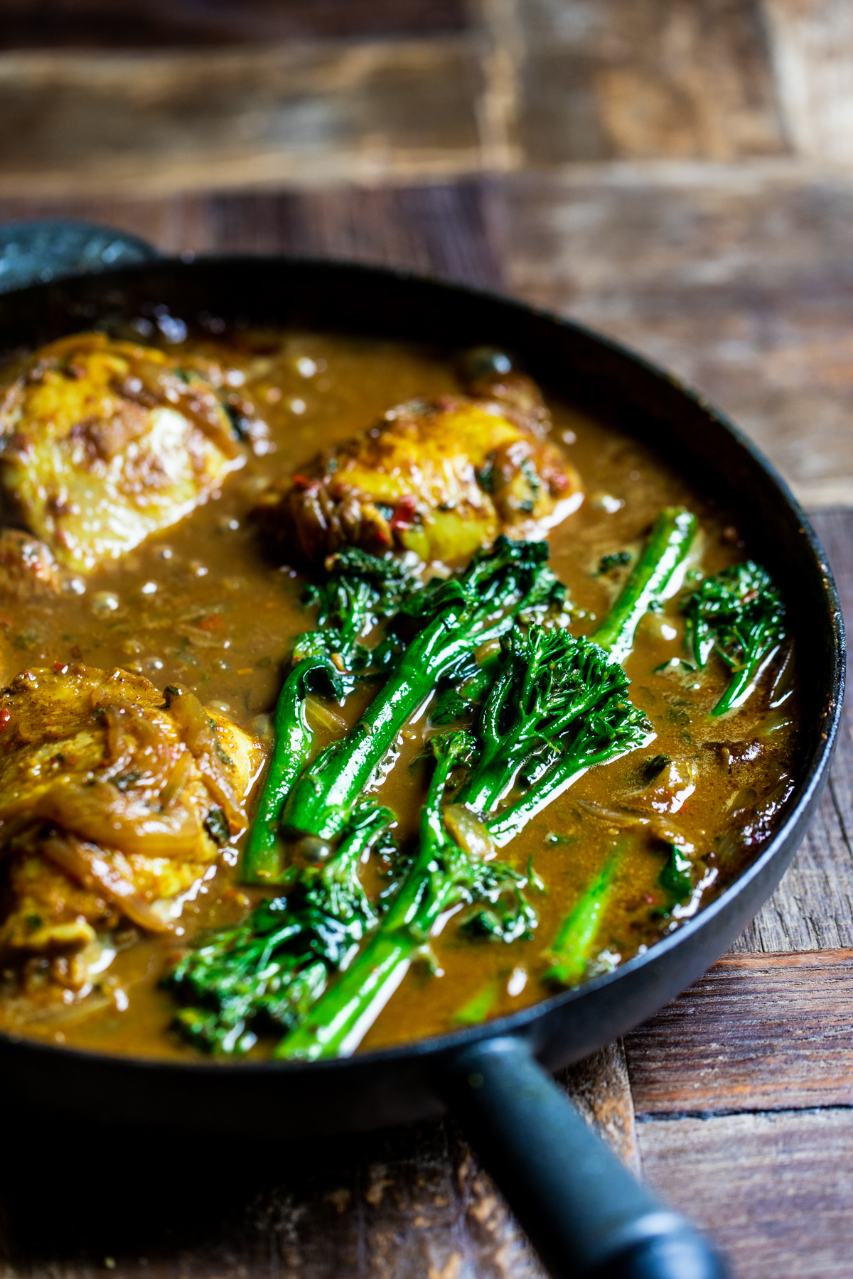 Malaysian chicken thigh curry cooking in a black cast iron pan with broccoli.