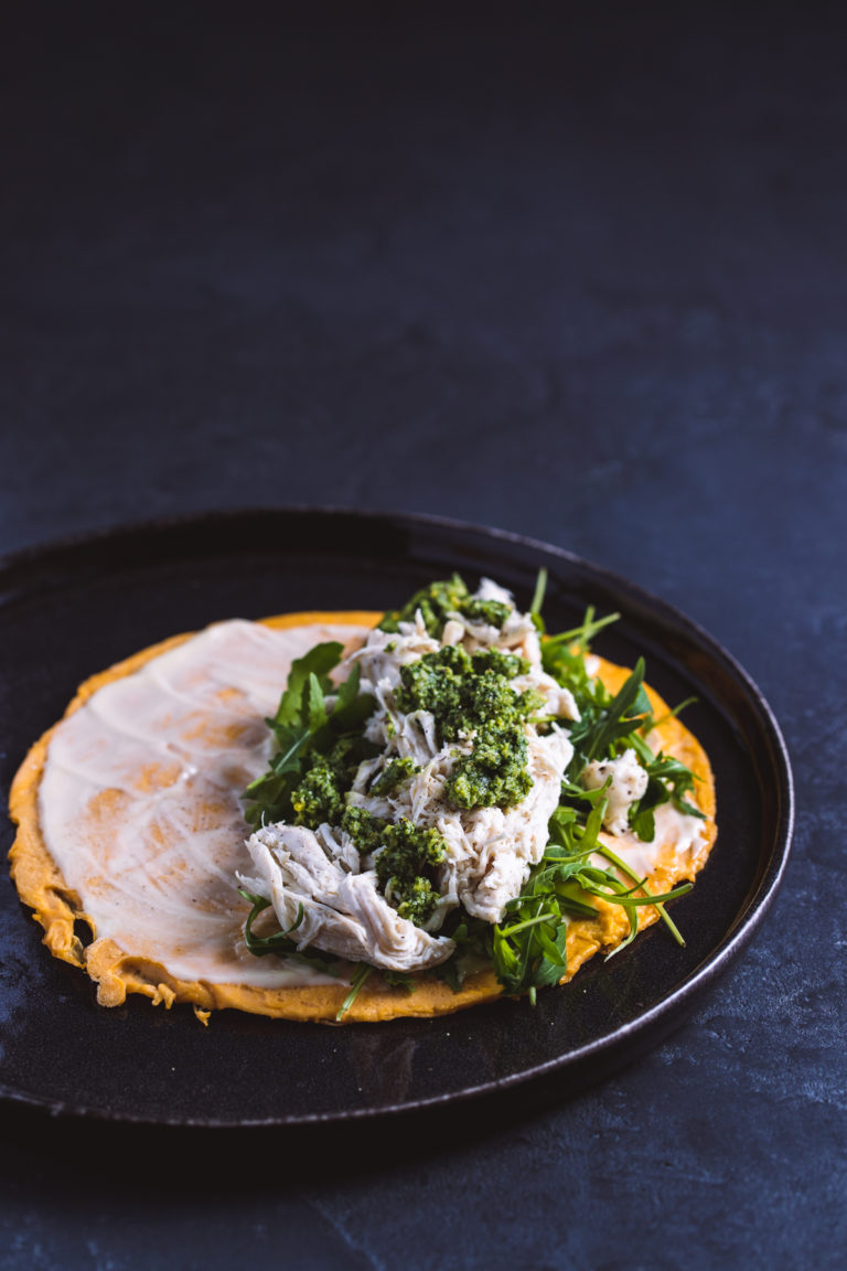 Chicken egg wrap with pesto and rocket on a black plate and black background.