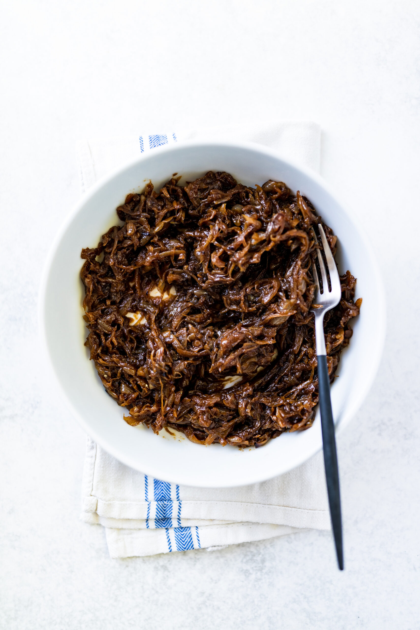 Caramelised onions in a white bowl on a tea towel and white background