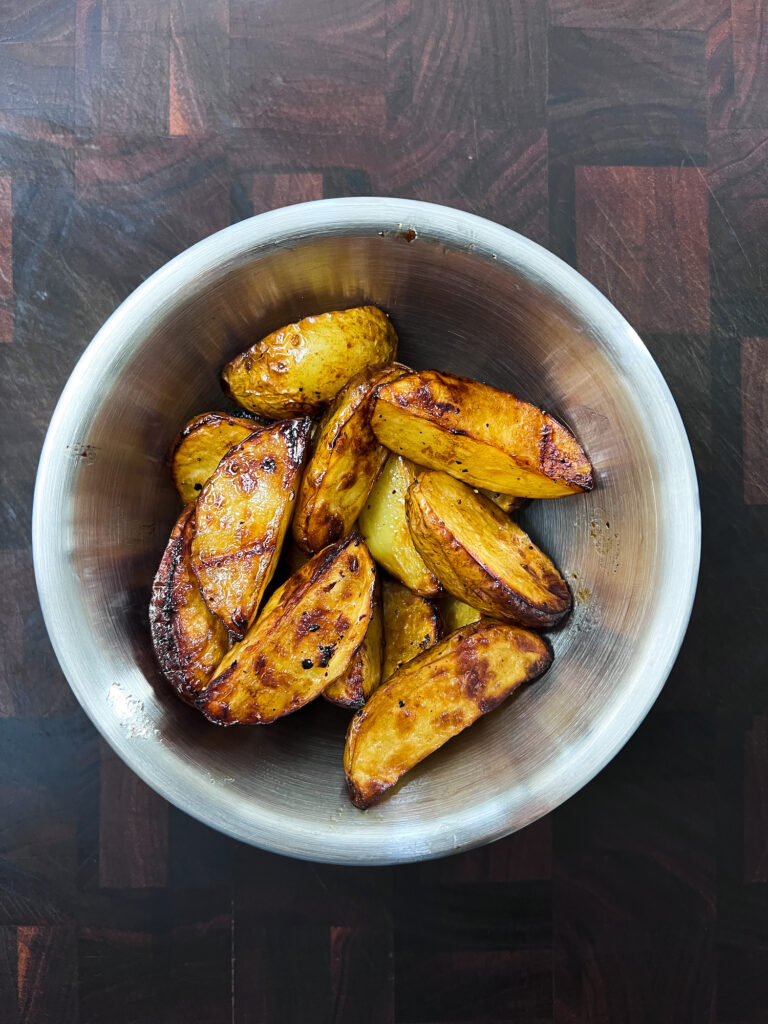 Air fryer balsamic potato wedges in a silver bowl on a wooden chopping board