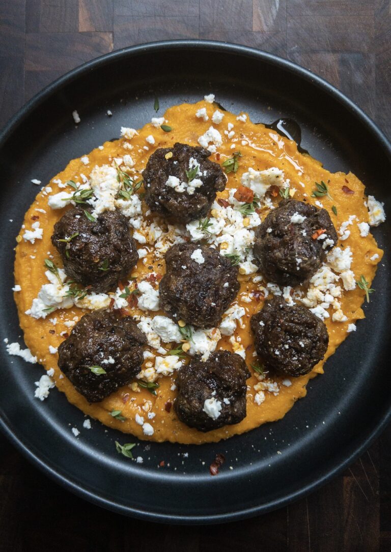 Overhead shot of beef and liver meatballs with sweet potato puree on a black plate