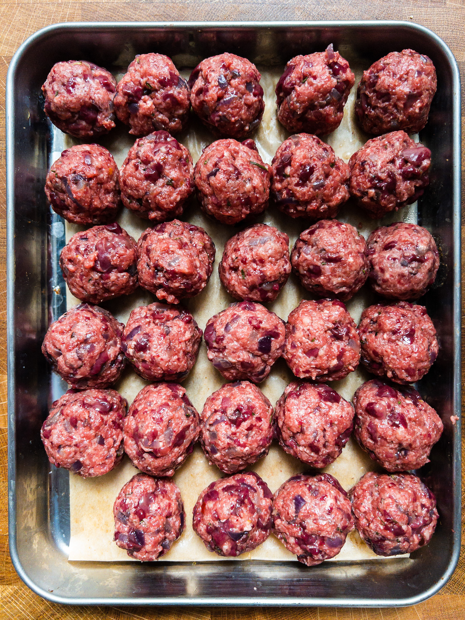 Overhead shot of a silver tray of uncooked liver and beef meatballs