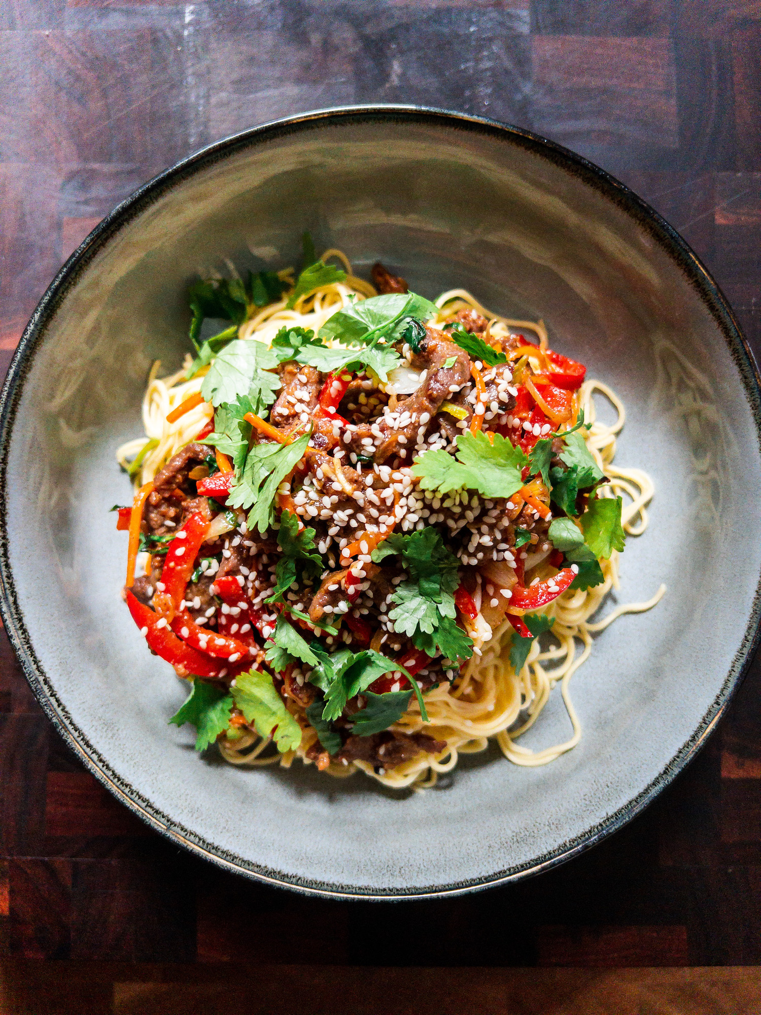 Overhead shot of beef stir-fry in a grey bowl on a wood background