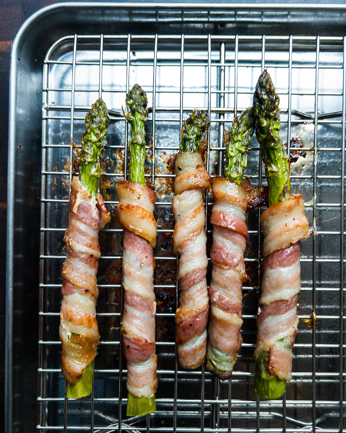 Overhead shot of bacon wrapped asparagus on a silver baking tray rack