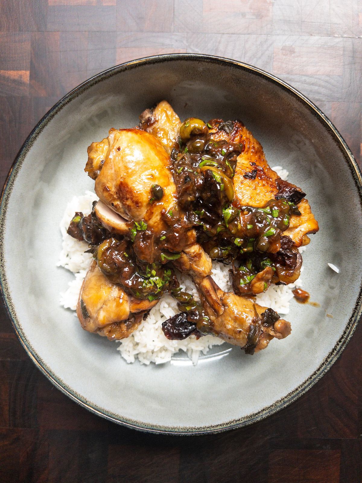Overhead shot of Chicken Marbella and rice in a grey bowl on a dark wood background