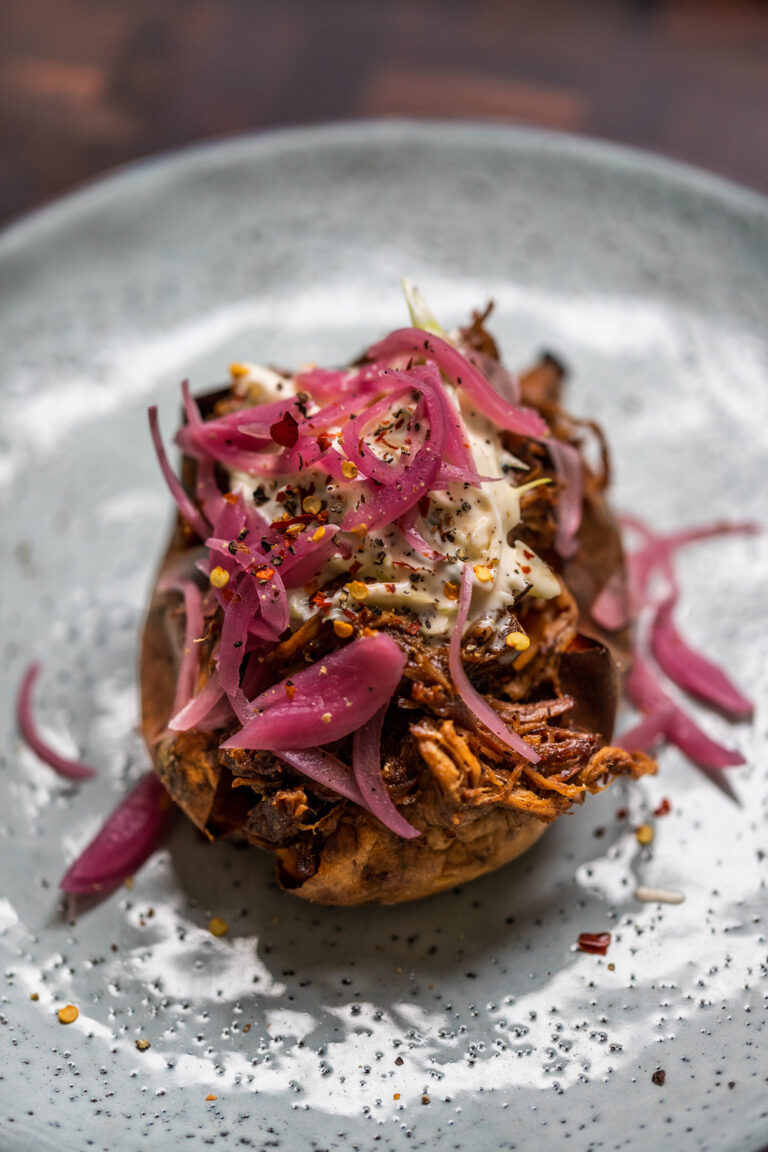 Smoky pulled pork baked sweet potato with crème fraîche and red picked onions on a blue plate