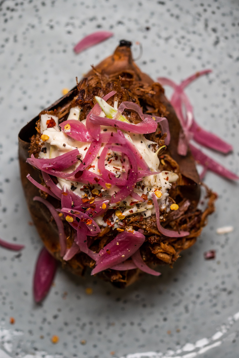 Smoky pulled pork baked sweet potato with crème fraîche and red picked onions on a blue plate