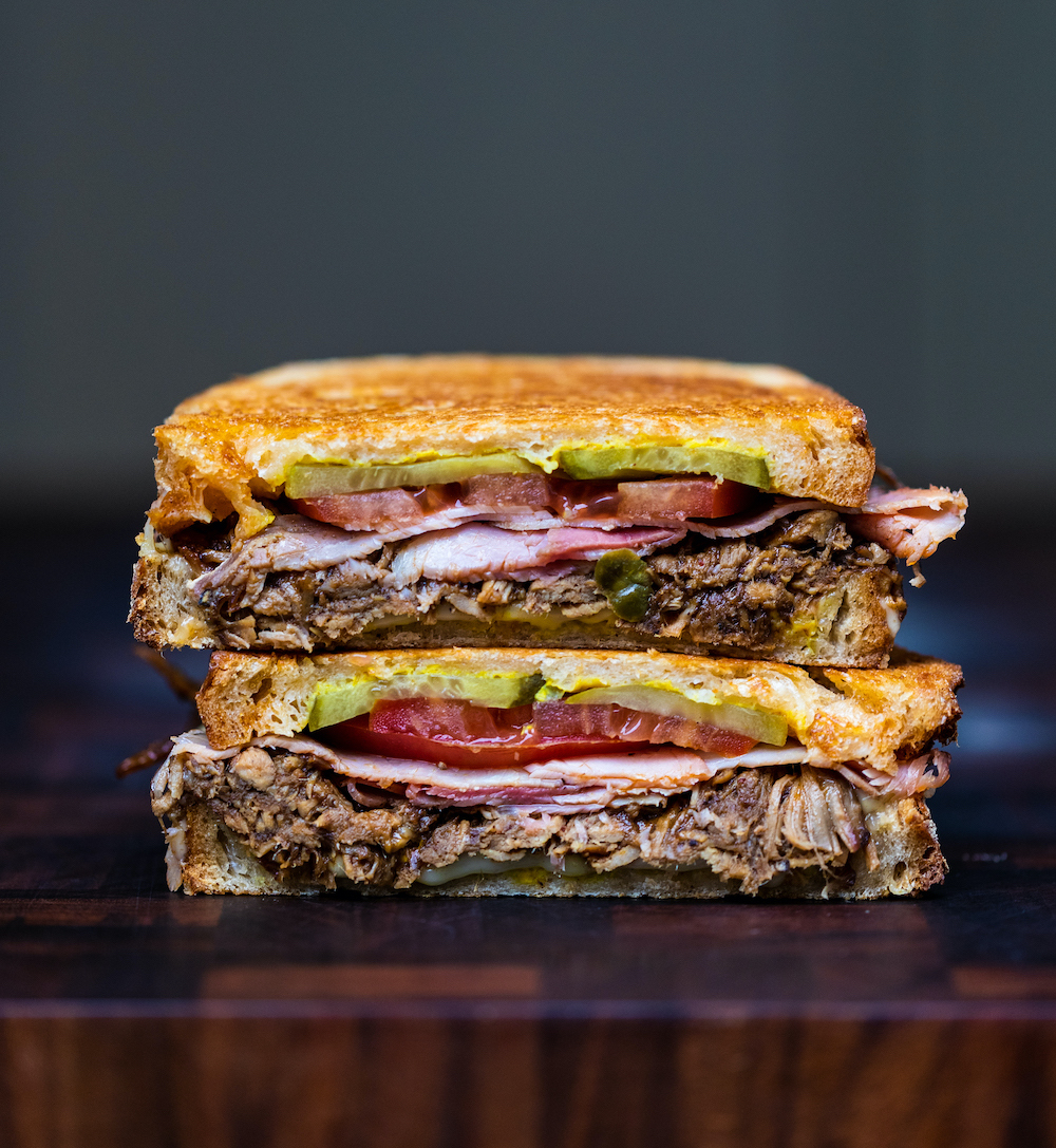 Cubano pulled pork sandwich cut in half with the two halves stacked on top of each other on a wooden chopping board