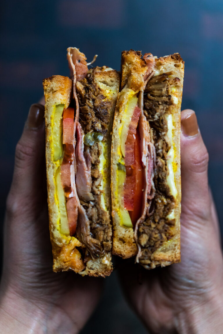 Cubano pulled pork sandwich cut in half being held next to each other by two female hands
