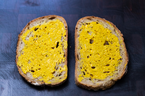 Two pieces of sourdough with mustard on a wooden chopping board
