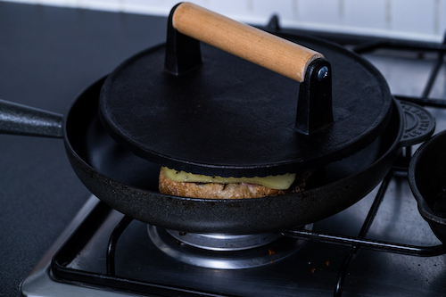 Cubano sandwich in a black cast iron pan with a burger press on top