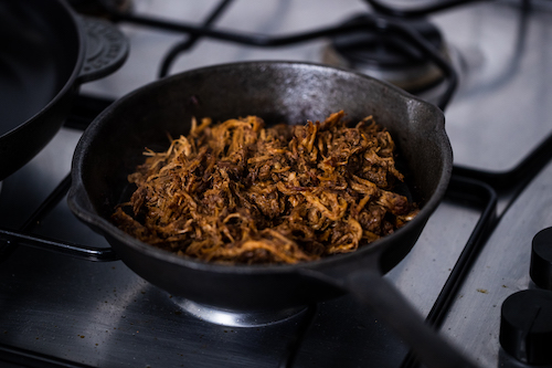 Smoky pulled pork in a black cast iron pan on a hob