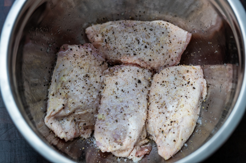 Skin-on chicken thighs with lemon, pepper and salt in a silver bowl