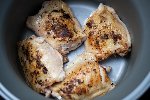 Seared skin-on chicken thighs in a slow cooker before cooking