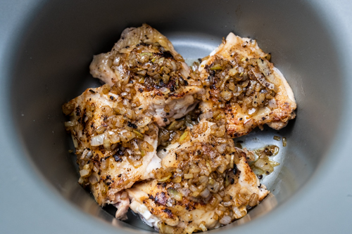 Seared skin-on chicken thighs with onion in a slow cooker before cooking