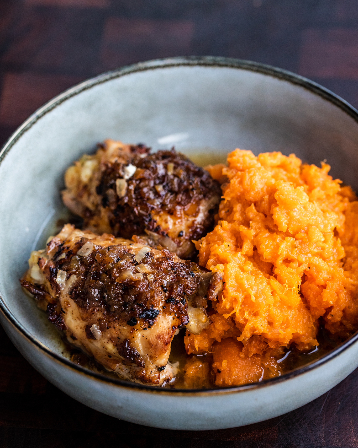 Slow cooked lemon chicken thighs with balsamic onions and sweet potato mash in a grey blue bowl on a wooden chopping board