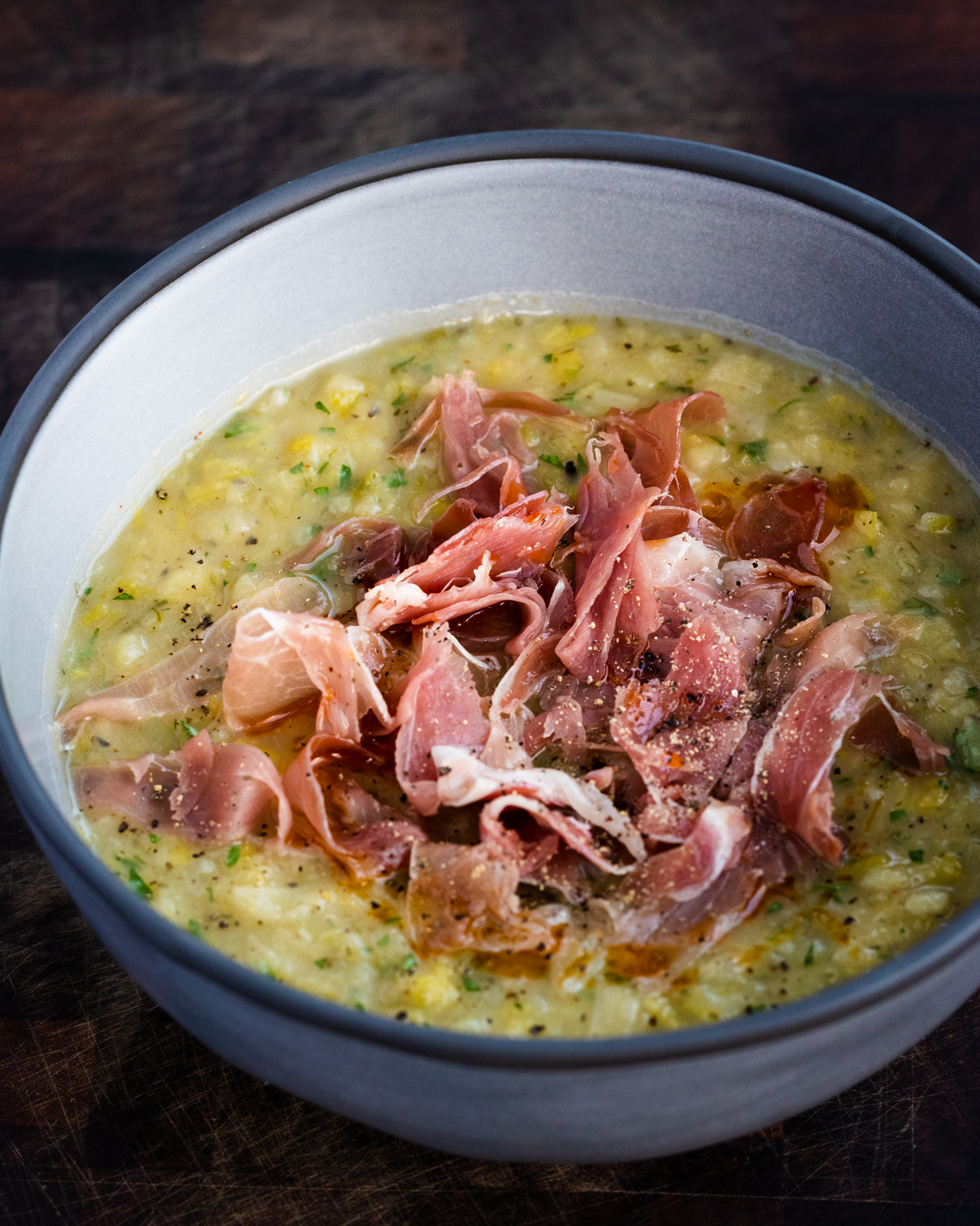 Leek and potato soup with no cream and serrano ham in a grey bowl on a wooden background