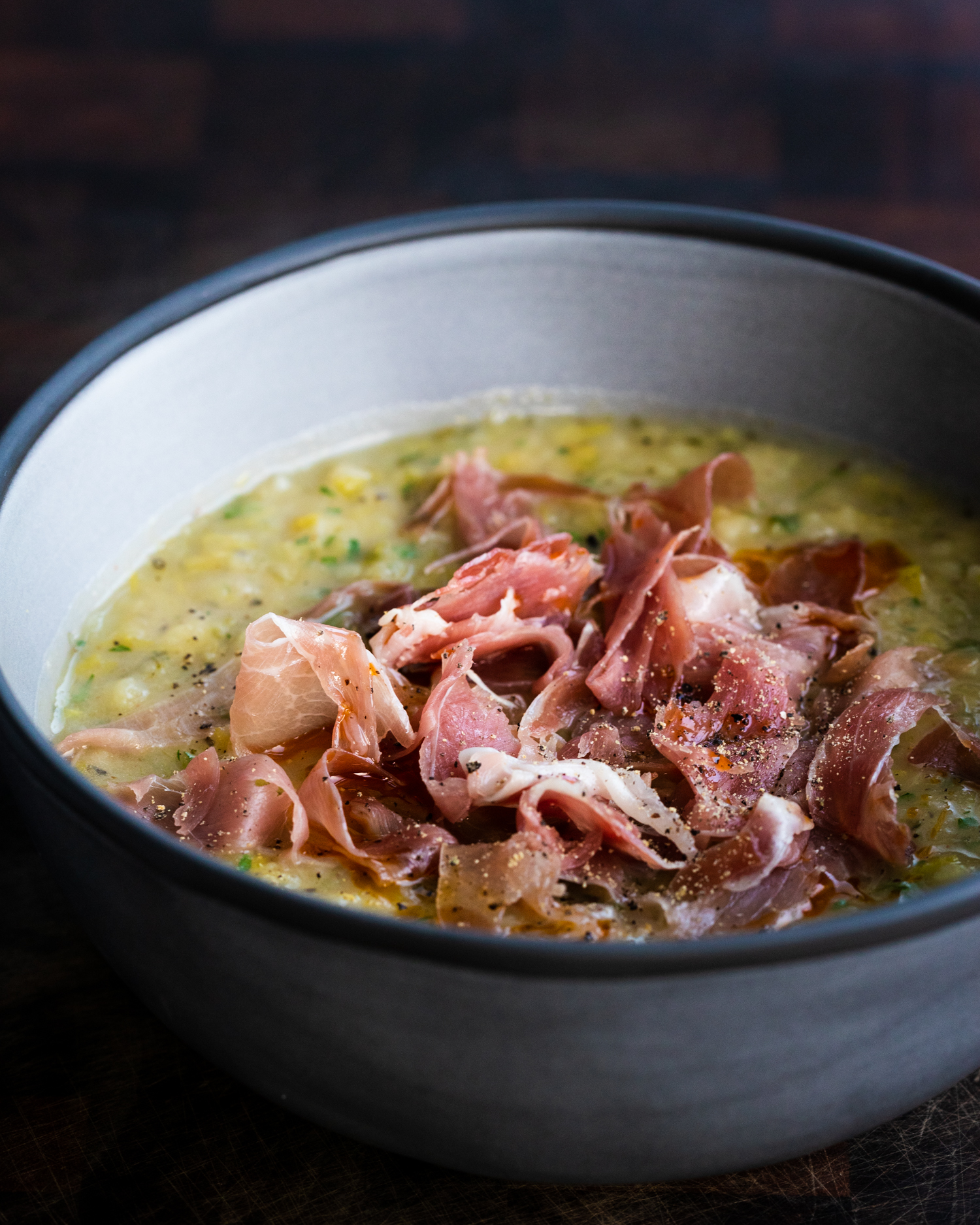 Leek and potato soup with no cream and serrano ham in a grey bowl on a wooden background
