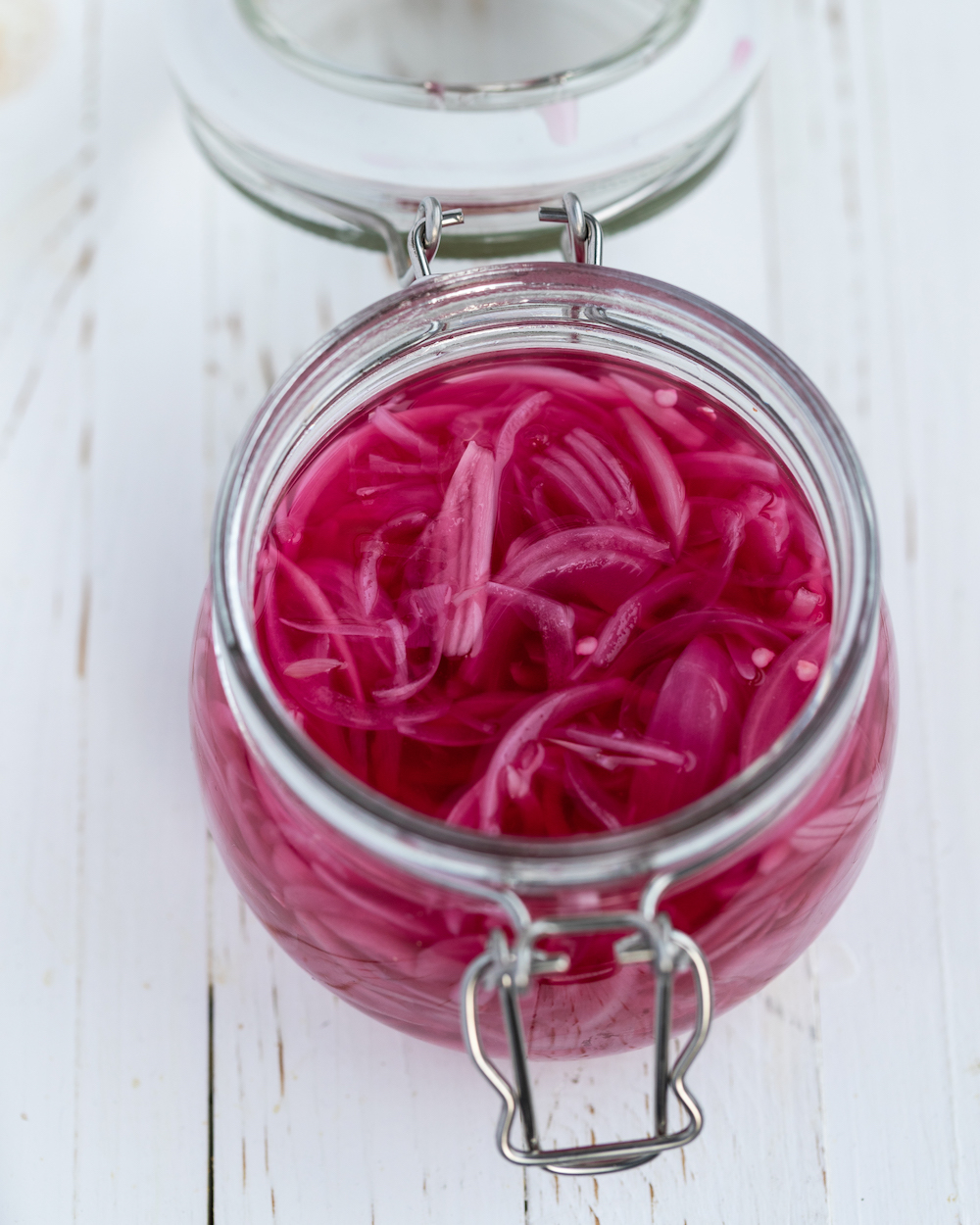 Quick pickled red onions in a glass jar on a white background