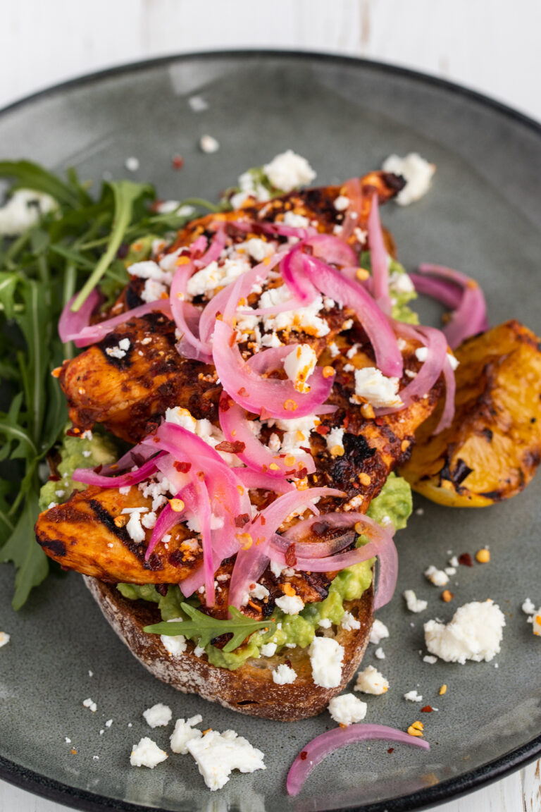 Grilled harissa chicken avocado toast on a grey plate and white background