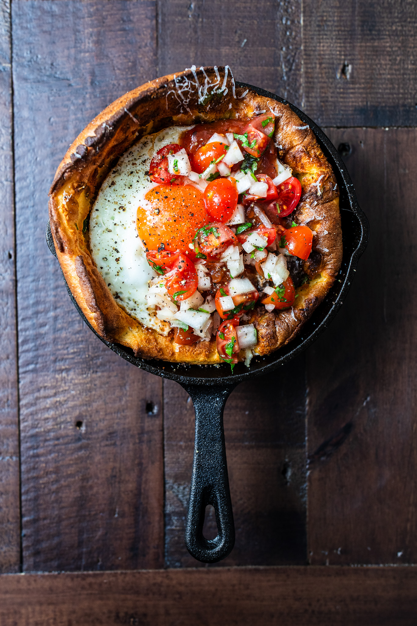 Overhead shot of a huevos rancheros savoury dutch baby in a skillet on a wooden table