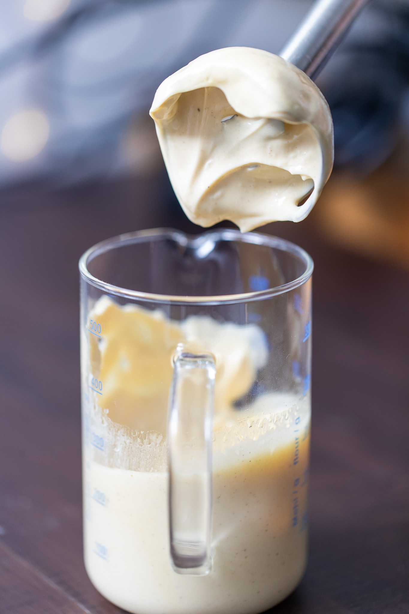 Creamy homemade olive oil mayonnaise in a glass jug with a hand blender being taken out