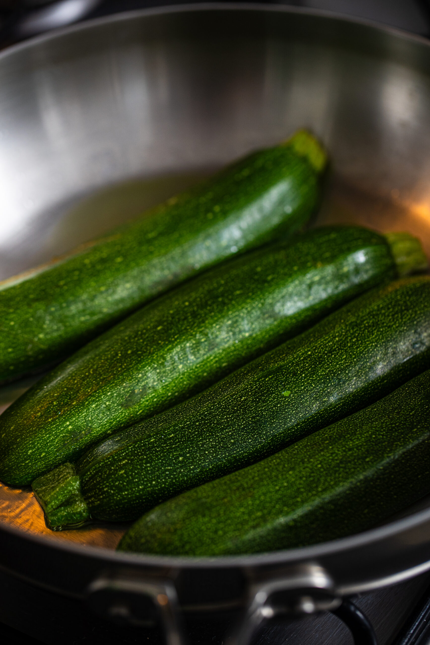 Zucchini being cooked cut side down in a stainless steel pan